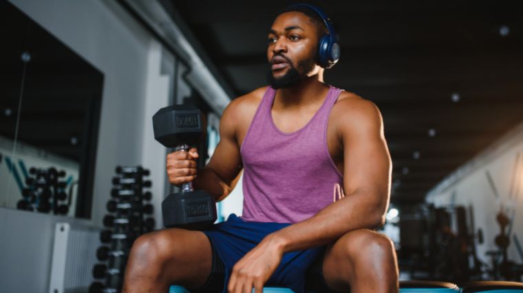 Person in pink tank top sitting on bench, resting a dumbbell on one thigh