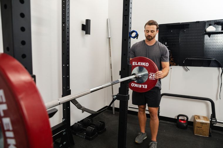 A young man putting a weight plate on a barbell on the Titan X-3 Power Rack