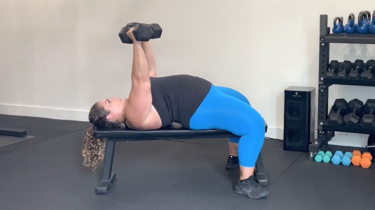 person in gym performing dumbbell bench press