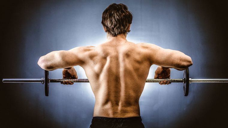 Muscular person lifting barbell to shoulders.