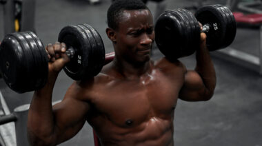 Muscular man performing seated shoulder press with dumbbells