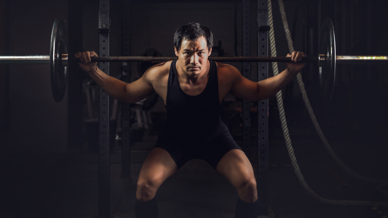 person in dark gym performing barbell squats