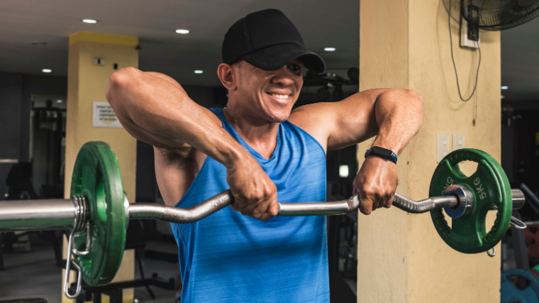 Muscular person in gym lifting barbell to shoulders.