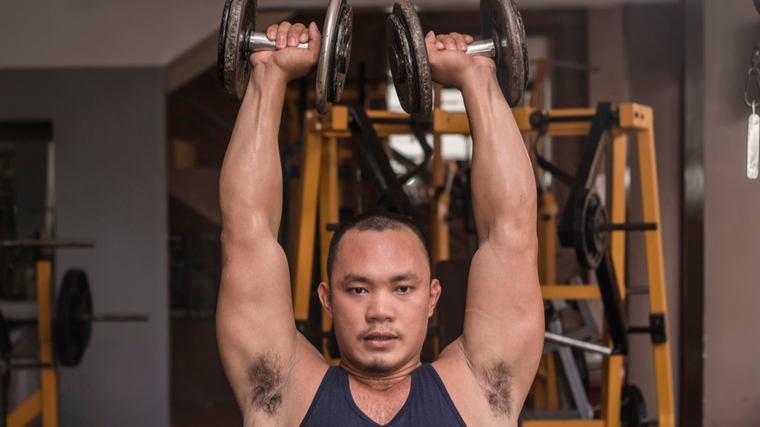 Man in gym pressing dumbbells overhead