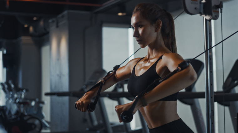 long-haired person in gym doing cable chest exercise