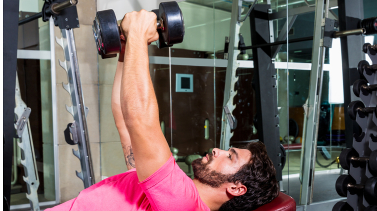 Man on bench in gym holding dumbbells overhead