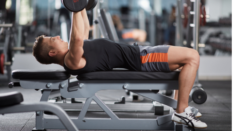 man in gym performing flat bench dumbbell press lifting head