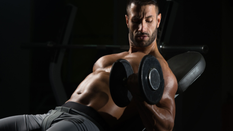 muscular person in dark gym performing dumbbell curl